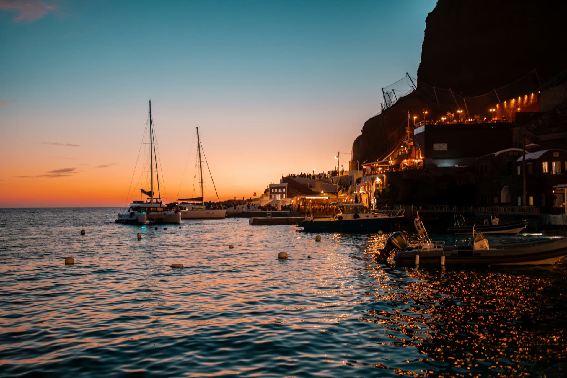 Sunset over Ammoudi harbour in Santorini with moored boats and warm terrace lights